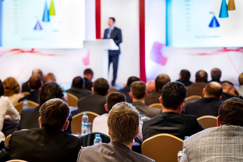 conference speaker at podium with large audience listening
